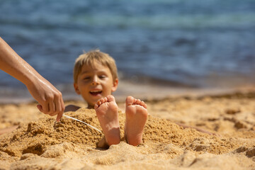Child, tickling sibling on the beach on the feet with feather, kid cover in sand, smiling, laughing