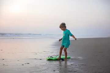 Happy children, boys, playing on the beach on sunset, kid cover in sand, smiling, laughing