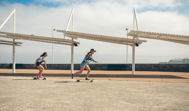 Two young women longboarding on beach promenade