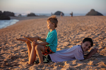 Child, tickling sibling on the beach on the feet with feather, kid cover in sand, smiling, laughing