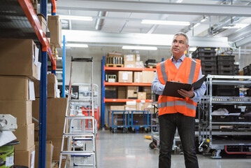 Man in factory hall wearing safety vest holding clipboard