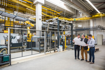 Three men with blueprint talking in factory shop floor