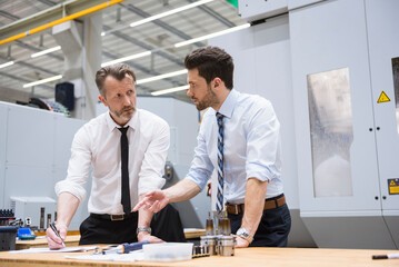 Two businessmen at table in factory shop floor discussing