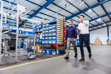 Two business people walking through shop floor. holding digital tablet