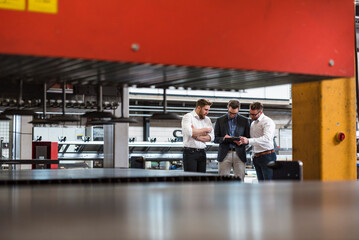 Three men sharing tablet on factory shop floor