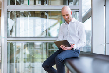 Smiling businessman sitting at the window using tablet