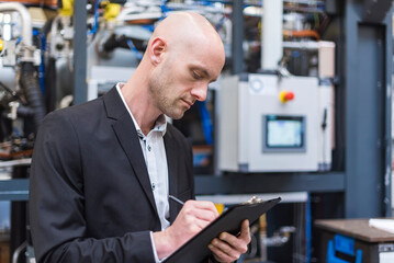 Businessman writing on clipboard in modern factory