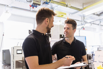 Two men with clipboard talking in factory
