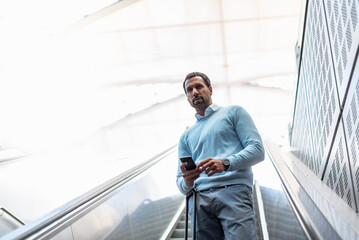 Businessman with smartphone on escalator