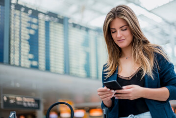 Young woman using cell phone at departure board looking around