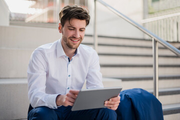 Smiling businessman sitting on stairs in the city using tablet