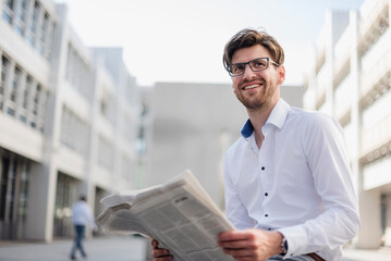 Smiling businessman sitting in the city reading newspaper