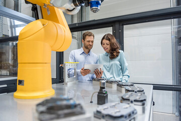 Colleagues in high tech company controlling industrial robots, using digital tablet