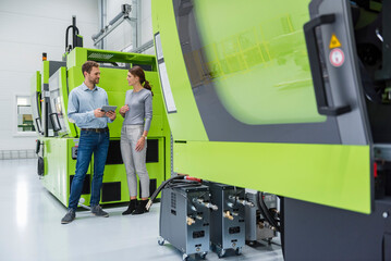 Colleagues in high tech company controlling manufacturing machines, using digital tablet