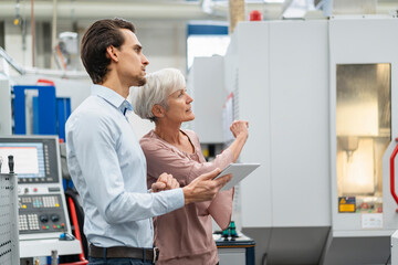 Businessman and senior woman with tablet talking in a factory