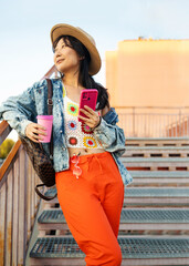 Image of fashionable Asian woman standing on street stairs on summer day holding coffee paper cup...