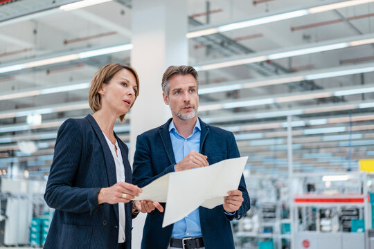 Businessman and businesswoman discussing plan in a factory hall