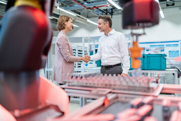 Businessman and businesswoman shaking hands in a modern factory hall