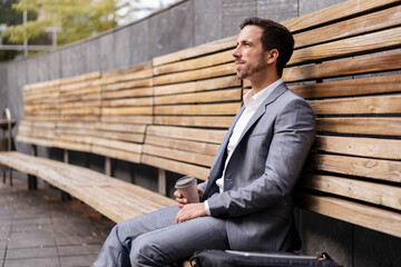 Relaxed businessman sitting on wooden bench in the city