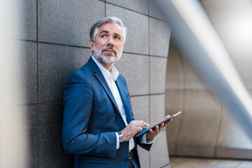 Mature businessman standing at a wall using tablet