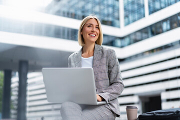 Smiling young businesswoman using laptop in the city