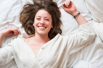 Cheerful young woman lying in bed at home