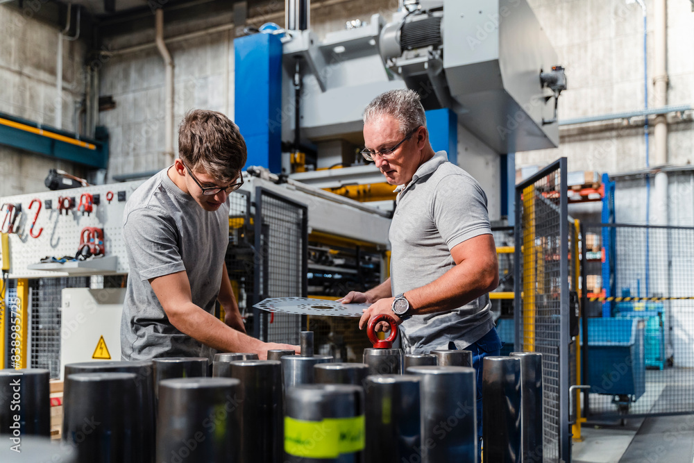 Wall mural male engineer examining product with mature technician in illuminated industry