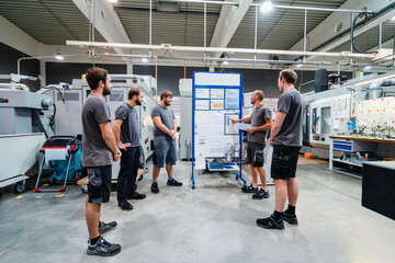 Maintenance engineers planning over chart on whiteboard while standing in meeting at industry