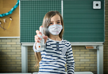 Portrait of girl wearing mask in classroom spraying sanitizer