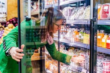 Woman taking packaged berries from cooling shelf in organic store