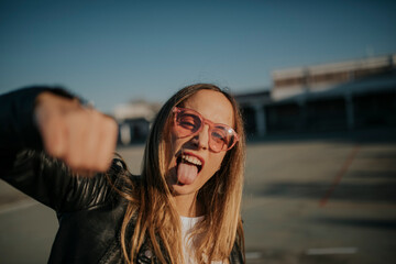 Portrait of young woman outdoors sticking out tongue and punching