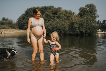 Netherlands, Schiermonnikoog, pregnant mother with daughter and Border Collie in a lake