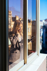 Young businesswoman standing at the window, talking on the phone