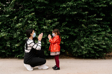 Mother and daughter wearing masks while playing clapping game on street