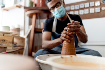 Male potter wearing mask molding shape to clay while sitting in workshop
