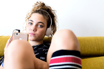 Portrait of girl sitting on the couch listening music with headphones and smartphone