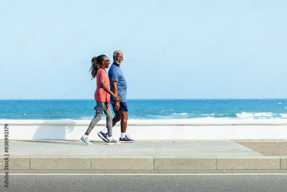 Wall mural Older couple enjoying a sunny walk by the sea