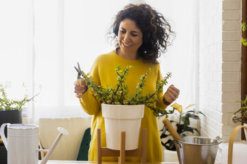 Woman at home wearing headphones and pruning plants
