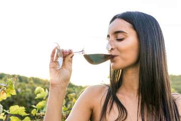 Italy, Tuscany, Siena, young woman drinking red wine in a vineyard at sunset