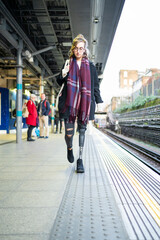 Young woman with leg prosthesis walking at station platfom