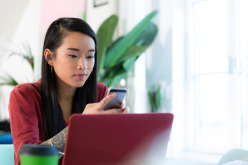 Woman using cell phone and laptop in office