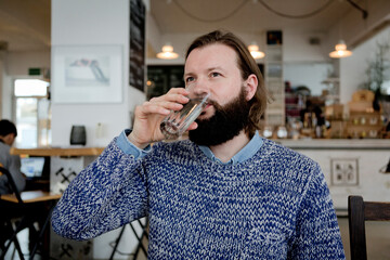 Man with beard sitting in cafe, drinking water