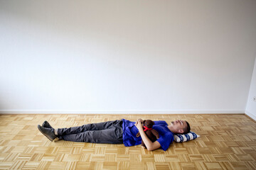 Young man laying on the floor in an empty apartment embracing a teddy bear