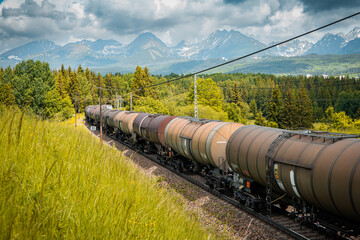 Transportation tank cars with oil during summer day. Railway containers. Freight railway wagons. Railway tank. Beautiful mountains landscape in background.