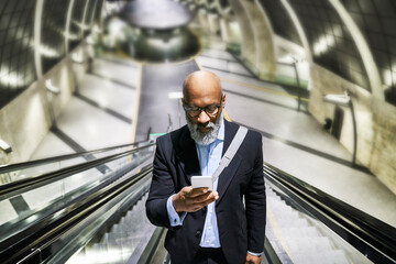 Businessman with smartphone reading messages on escalator