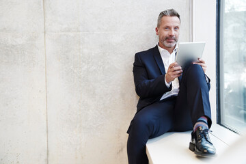 Portrait of smiling businesssman using tablet at the window