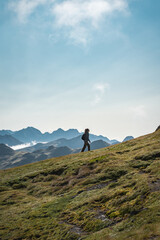 Obraz premium A person is walking up a grassy hill in the mountains under a cloudy sky, surrounded by lush greenery with a vast landscape spreading in the horizon