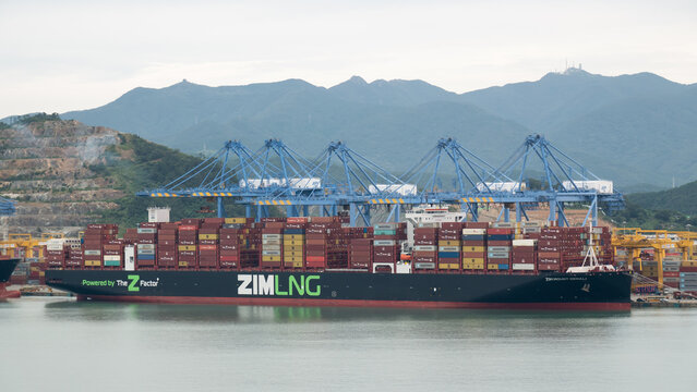 Busan, South Korea - 10.01.2023: ZIM Mound Denali LNG fuel powered vessel has cargo operations in container terminal of port New Busan in stead of living buildings of Busan city 