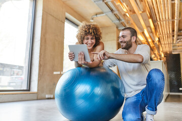 Happy man and woman using tablet on fitness ball in modern office