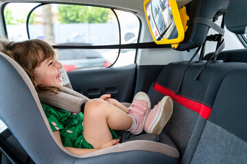 Laughing toddler girl sitting in a car seat looking in a mirror